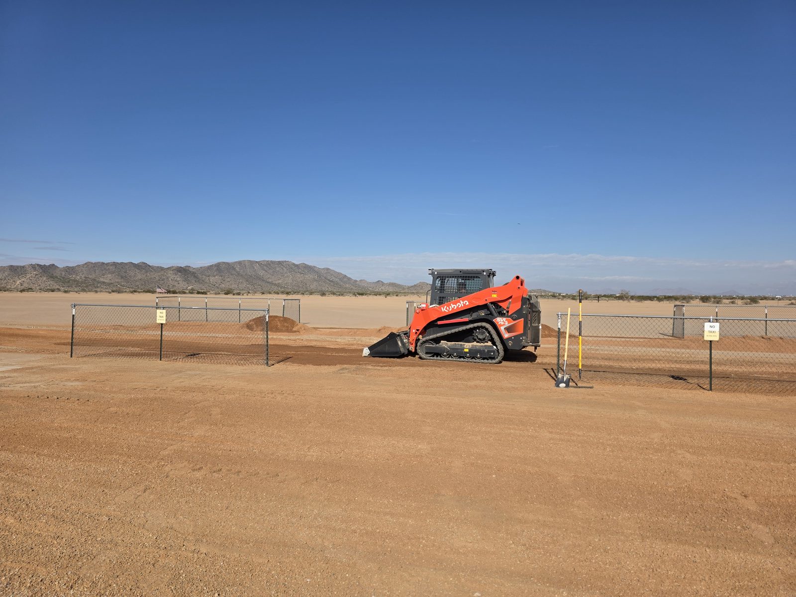 Kubota SVL75-3 track loader grading near the chain-link fence at the club pit area