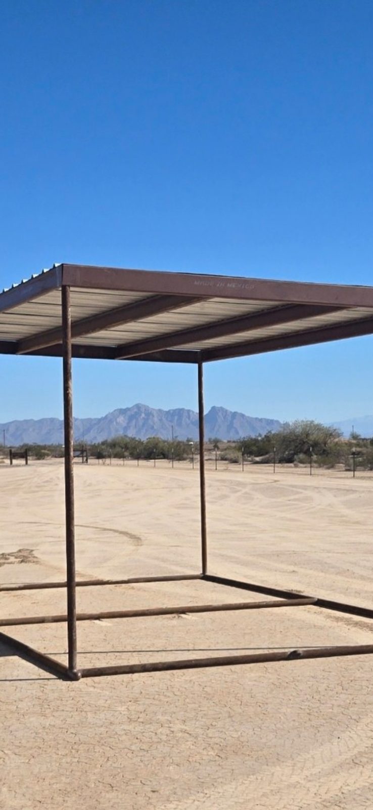 Metal sun shade frame and roof standing alone on the desert field with mountains behind